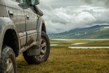 A dirty off-road vehicle with off-road tires, stands beautifully in a yellow clearing with a view of the mountains and the sky. Demonstration of an off-road wheel.