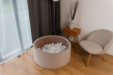 Modern Home Interior with Beige Ball Pit Filled with White Balls Near Window Curtain, Wooden Side...