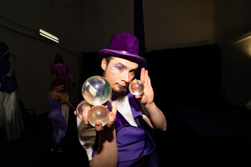 Male artist juggling crystal balls on stage during a vibrant circus show, dressed in a striking...