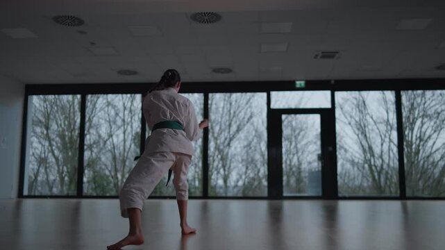 Woman training Karate in the dark, with big windows in the back