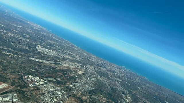 An aerial panoramic view of Valencia city, harbor and airport, taken from an airplane cockpit doing a left turn under a bright sunny day.