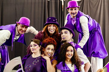 Group of smiling circus performers wearing purple costumes and stage makeup posing together for a portrait