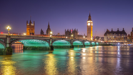 Fototapeta premium The Houses of Parliament and Big Ben glow against the night sky, with Westminster Bridge elegantly lit. The tranquil river reflects the lights, showcasing London's iconic architecture.