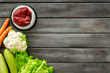 Natural pet food in feeding bowl and ingredients meat and vegetables, top view