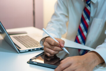 person in formal attire using stylus on tablet, with laptop in background, suggesting professional and modern workspace