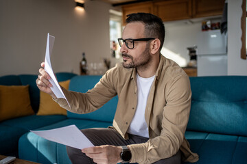 Focused man reading documents at home on sofa in living room