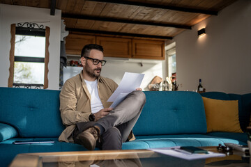 Focused entrepreneur reading documents on sofa in home office