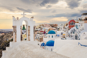 Scenic view of Oia, Santorini, Greece, featuring the iconic three domes viewpoint, colorful houses, and the Aegean Sea. Horizontal shot with a cloudy sky, perfect for honeymoon or wedding destination