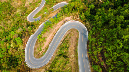 Aerial top down bending curve winding road path in the green forest 
