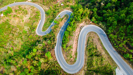 Aerial top down bending curve winding road path in the green forest 