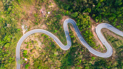 Aerial top down bending curve winding road path in the green forest  © Michele