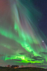 Beautiful Aurora Borealis over house on island of Hillesøya, dancing northern lights with clear colorful rays of green light in the sky with red and purple strikes! amazing joy in Norway