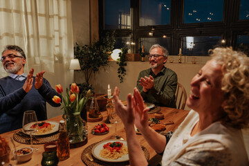 Group of senior adults celebrating with a dinner at home applauding after a speech