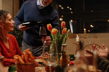 Senior man pouring red wine for his wife during romantic pension celebration dinner