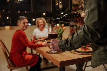 Waiter pouring red wine for senior friends celebrating pension