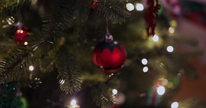 Festive close-up shot of a decorated Christmas tree with a shiny red bauble ornament hanging from a branch. 