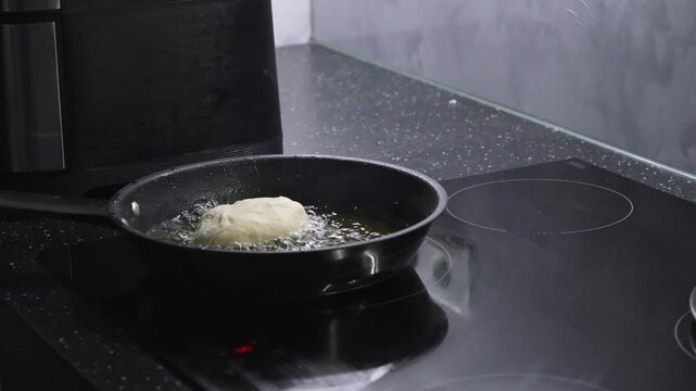 placing a raw dough pastry into hot oil in a frying pan for deep frying, preparing a crispy and golden-brown savory treat