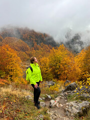 A tourist stands in a bright autumn forest and mountains and looks up