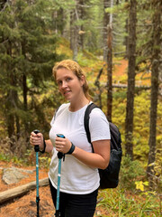 Middle aged woman standing on forest path with backpack and trekking poles, active lifestyle