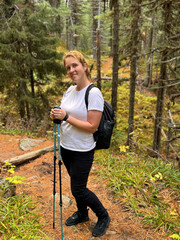 Middle aged woman standing on forest path with backpack and trekking poles