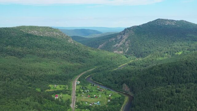 Aerial view of Aygir village in Ural mountains. Camera pans over a stunning mountain valley featuring houses and a river flowing through the lush landscape