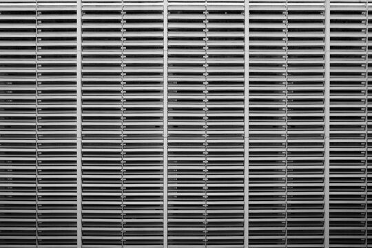 A black and white image showcasing a tightly cropped, symmetrical view of a large metal vent or louver system.  - Powered by Adobe