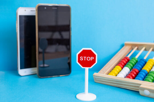 Road stop sign with defocused smartphones and abacus on blue background, digital screens and children addiction problem, abstract metaphor