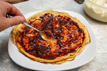 Spreading plum jam on pancakes with a silver teaspoon, soft focus close up