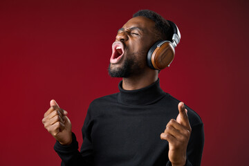 Young Black man enjoying music with headphones, expressing joy and excitement in a vibrant red...