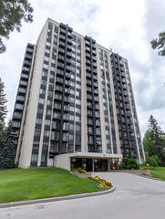 Tall residential apartment building with white and dark vertical panels balconies green lawn and curving driveway.