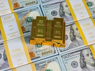 Gold bars stacked on top of a spread of hundred dollar bills in a financial