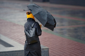 Woman struggles against strong wind and rain, gripping an umbrella as it bends under force of storm while walking down wet city street. Woman fighting against the rain and wind, gusts on stormy day
