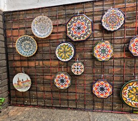 A vibrant display of traditional decorative ceramic plates with a typical traditional Andalusian style hanging on a metal grid in the historic streets of Seville. Spain