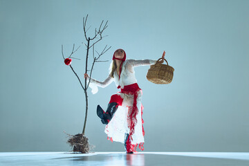 Woman in fluid motion, holding basket, posed beside bare tree with blooming rose, symbolizes...