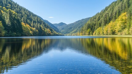 Fototapeta premium Serene mountain lake reflecting autumn foliage under a clear blue sky. The still water mirrors the surrounding hills and trees, creating a symmetrical and peaceful scene.