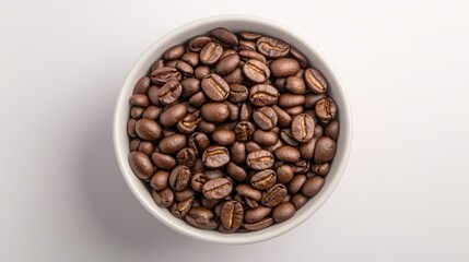 Fototapeta premium Overhead shot of a white bowl filled with dark roasted coffee beans against a bright white background.