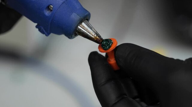 Applying adhesive with a glue gun: Close-up of gloved hands using a glue gun for precise application, highlighting craft or repair work in detail