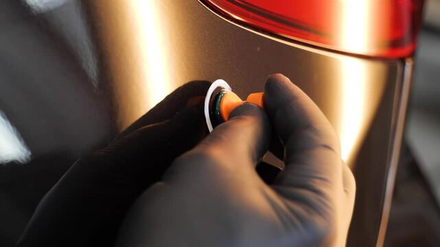 Auto body dent repair: Close-up of gloved hand attaching a tab to a car panel, highlighting the paintless dent removal process and automotive skill