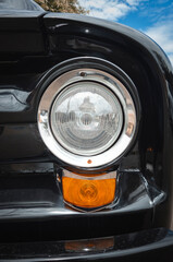 Close-up of the headlight and turn signal of a black vintage car with a shiny chrome finish.