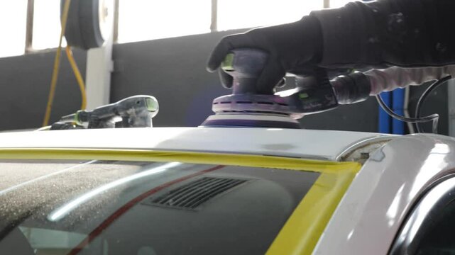Car body sanding: Close-up of gloved hand using an orbital sander to smooth a car surface, focusing on auto repair and bodywork processes