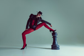 Woman in gothic fashion and surreal styling reclines on chess piece, transforming game into artful abstraction. Concept of beauty, fashion, confidence, performance, mental strength, surreal.
