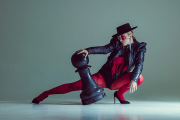 Woman dramatically leaning on fallen chess piece, red tights and black outfit accentuating tension...