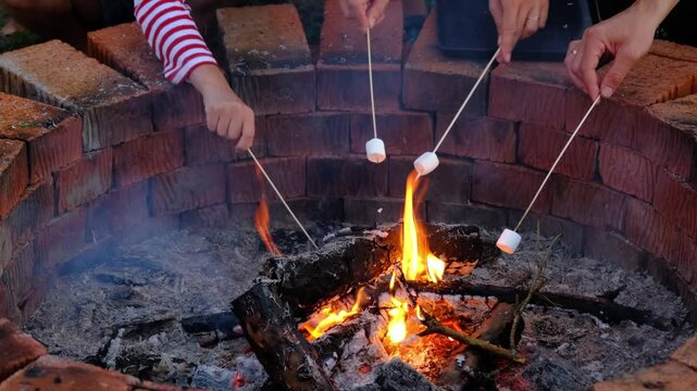 Roast marshmallows on a stick on skewers on a campfire in the hearth in the courtyard of the house by the fire pit on a cozy summer evening.