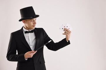 Illusionist pointing magic wand on playing cards against white background. Space for text