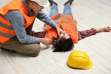 Accident at work. Man checking pulse of his unconscious colleague in warehouse