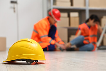 Accident at work. Hardhat on floor and man helping his injured colleague in warehouse, selective...