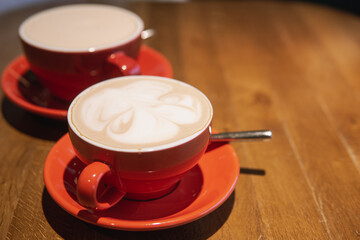 Artistic latte creations served in red cups on a wooden table. A perfect representation of a cozy cafe atmosphere for coffee lovers.