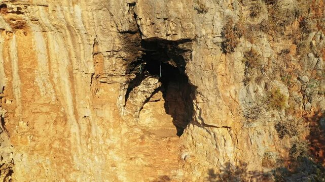 Aerial view of sunlit cave entrance with textured rocks, illuminated in warm colors in Kas, Tukey. Lycian path