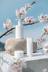 White skincare bottles on stone with cherry blossoms and sky