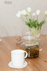 A peaceful arrangement featuring a glass teapot, cups, and a vase of white tulips on a wooden table, evoking warmth, simplicity, and serenity in the decor.